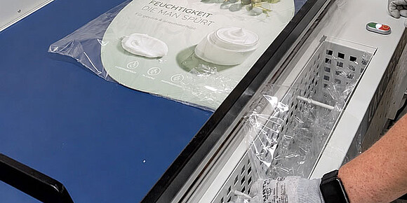 Verpackungsmaschine foliert ein ovales Werbeschild mit der Aufschrift Feuchtigkeit die man spürt.